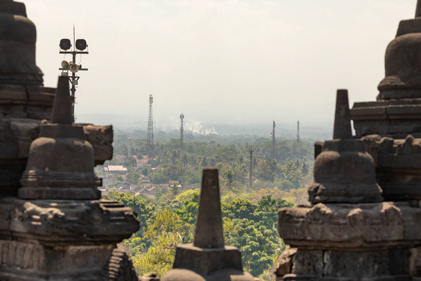 Detalles de varias estupas que coronan las balaustradas y paredes de los diferentes niveles del templo Borobudur en Java Central, Indonesia, en el fondo, fragmentos del paisaje circundante
. - Foto, imagen