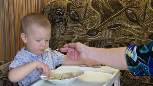 Pikkulapsi ruokki ruokaa pienessä pöydässä - Materiaali, video