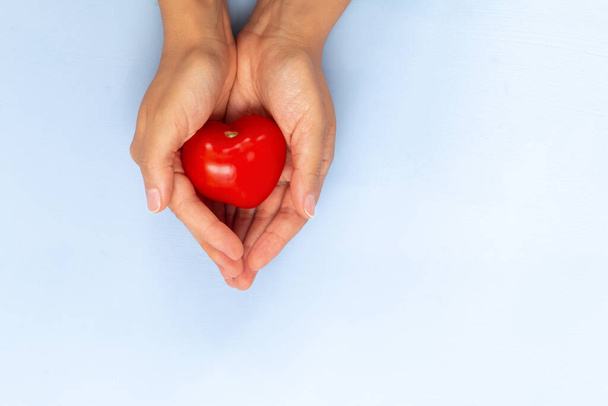 vermelho pequeno tomate em forma de coração em mãos no fundo azul claro, espaço vazio para texto
 - Foto, Imagem