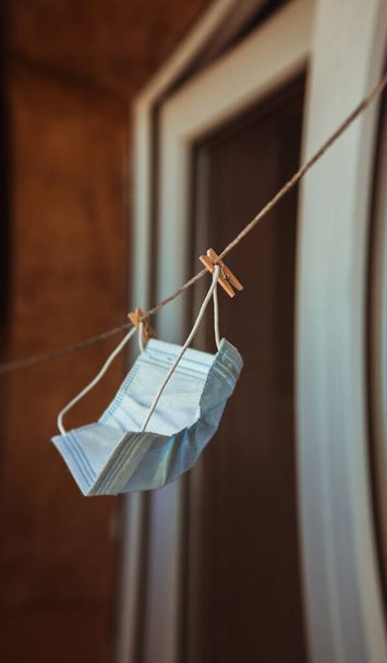 A white medical protective mask hanging is dried on the balcony next to the washed laundry. - Photo, Image