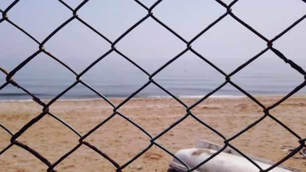 metal netting grill. Sandy seashore clear blue sea. View of beach through fence - Footage, Video