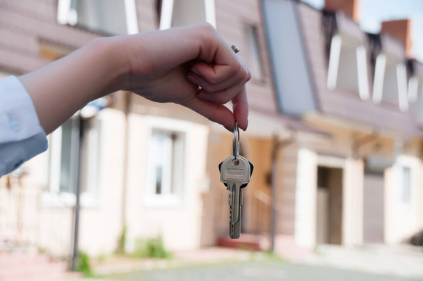 Ключи от квартиры в женской руке на фоне красивых новых двухэтажных домов в городе
 - Фото, изображение