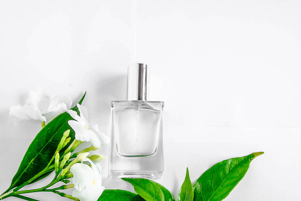 Parfum fles en witte bloem met groen blad op witte achtergrond. - Foto, afbeelding
