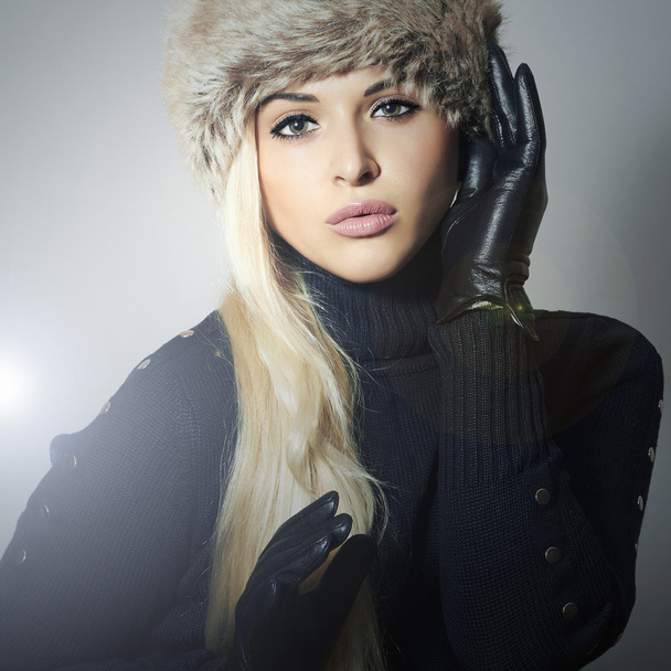 Beauty Fashion blond Girl in Fur Hat. Beautiful Blond Woman in Leather Gloves. Black sweater. Winter Fashion. Gray Background - Photo, Image