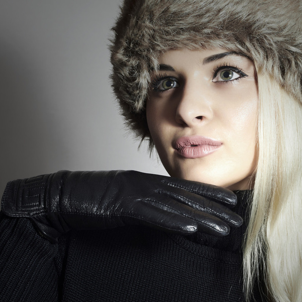 schoonheid mode blond meisje in bont hoed. mooie blonde vrouw in lederen handschoenen. zwarte trui. winter mode - Foto, afbeelding