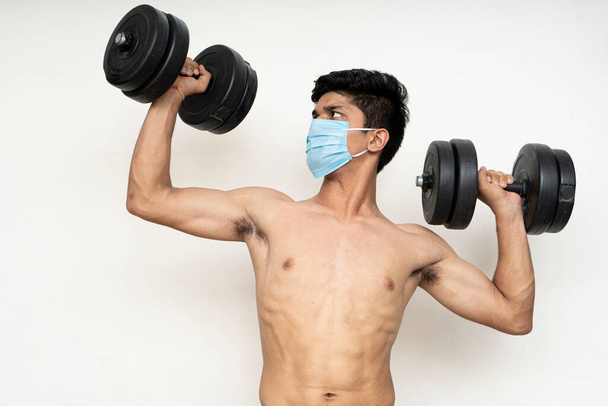 Fitness muž s maskou pro ochranu proti epidemii pracovní cvičení pro paže, bicepsy a ramena s činkami. - Fotografie, Obrázek