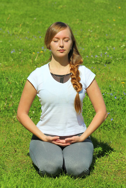 Young woman of European appearance does yoga in summer nature. Woman sitting in hero pose, virasana. High quality photo for web and print with empty space for text and design. - Фото, изображение