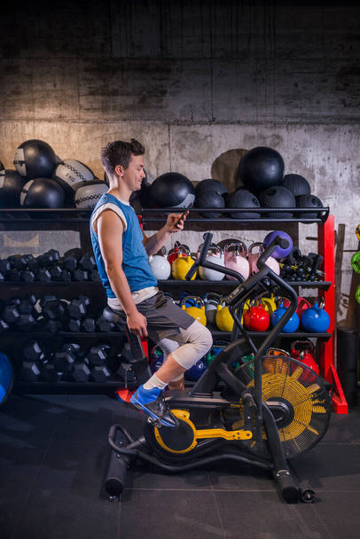 Young male exercising alone indoors, using his mobile phone to connect with his personal trainer during covid19 pandemic. - Photo, Image