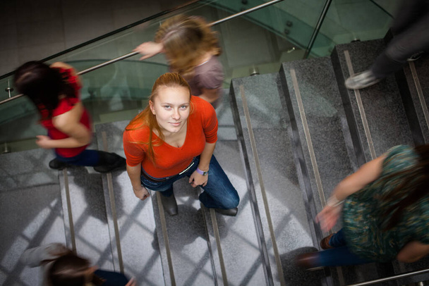 At the university/college - Students rushing up and down a busy stairway - confident pretty young female student looking upwards - Photo, image