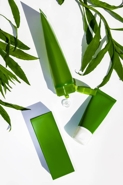 Un tube de vert avec un gel transparent d'aloe vera. Sur fond blanc parmi les feuilles vertes - Photo, image