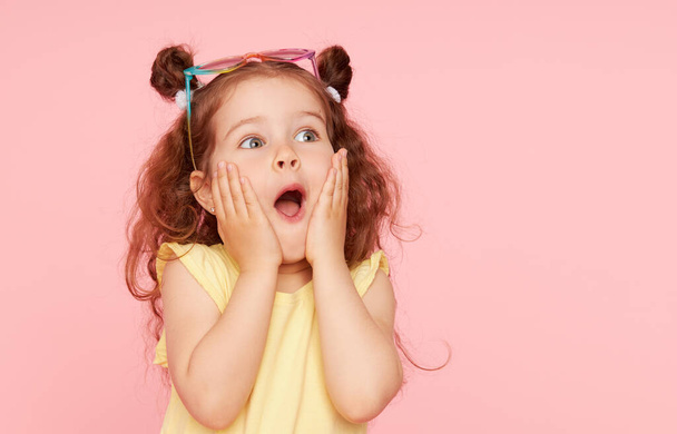 Portrait of surprised cute little toddler girl  in sunglasses over pink background.  Child model have fun and jump. Advertising childrens products - 写真・画像