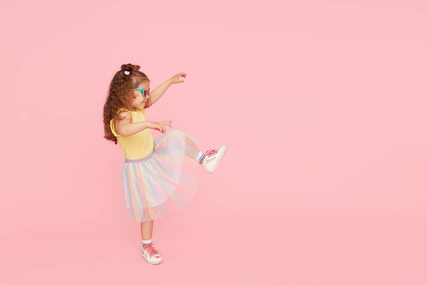 Portrait of surprised cute little toddler girl  in sunglasses over pink background.  Child model have fun and jump. Advertising childrens products - Φωτογραφία, εικόνα