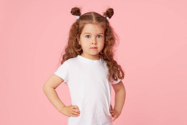 Retrato de linda niña europea sobre fondo rosa. Mirando la cámara. Modelo infantil en camiseta blanca. Publicidad productos para niños
 - Foto, Imagen