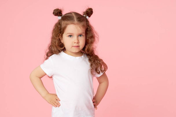 Portrait of cute european little toddler girl over pink background. Looking at camera. Child model in white T-shirt. Advertising childrens products - Foto, Imagen