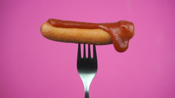 Ketchup oder rote Soße auf Wurst verteilen. Wurst auf Gabel auf rosa Hintergrund - Filmmaterial, Video