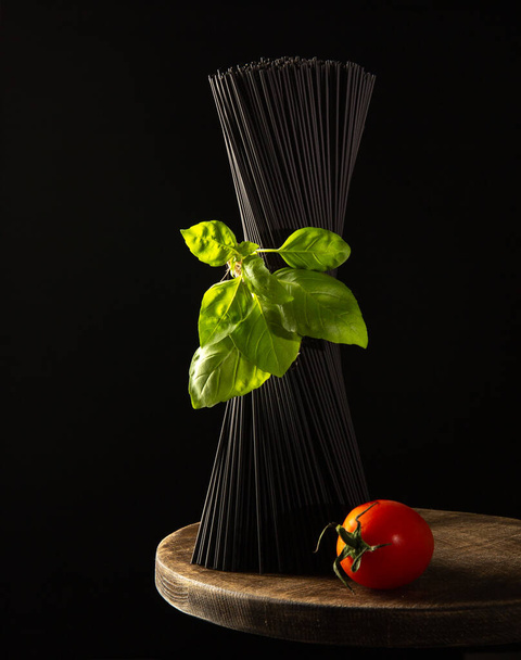 Black raw Spaghetti on wooden table with fresh Basil leaves and ripe cherry tomato.Close-up. - Fotoğraf, Görsel