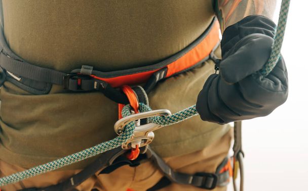 Unrecognizable sporty climber man in safety harness and gloves belaying with rope and figure eight device indoor, close-up. - Foto, immagini