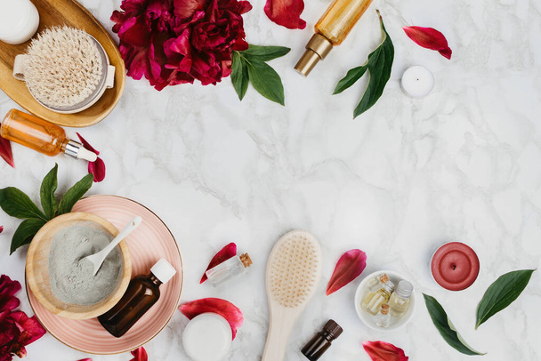 Flatlay of various beauty, bath and SPA products (serum, clay, essential oils, body brush, cream etc) and peony flower and petals on a marble background - Zdjęcie, obraz