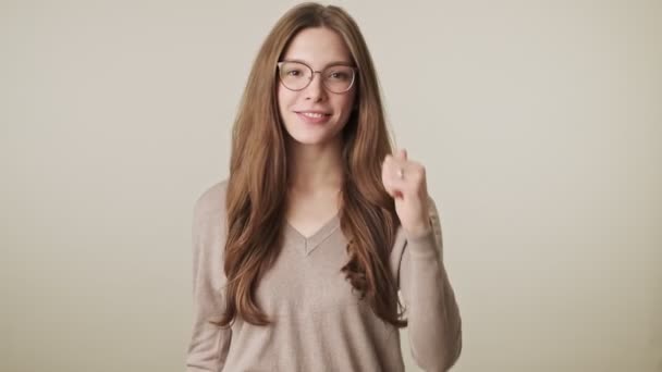 Beautiful young cheerful pretty woman wearing glasses isolated over grey wall background showing thumbs up gesture - Video