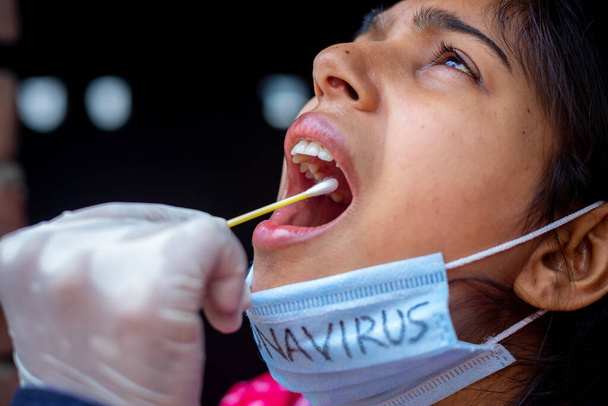 La mano del dottore che fa il test della saliva dalla bocca di una giovane donna con Cotton Swab. Coronavirus Raccolta campioni di gola. Osservazioni ravvicinate
. - Foto, immagini