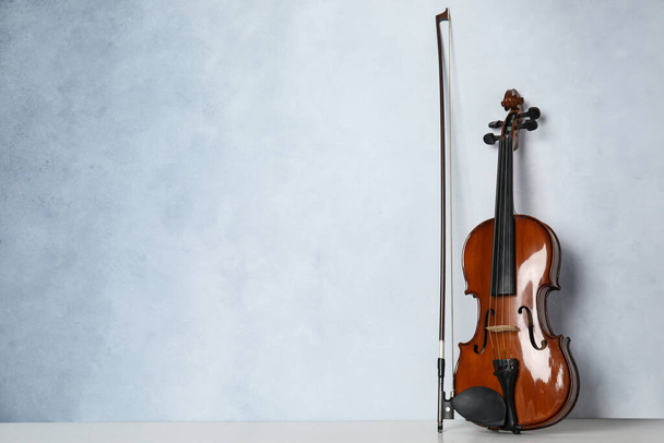 Beautiful violin and bow on table near light blue wall. Space for text - Foto, afbeelding