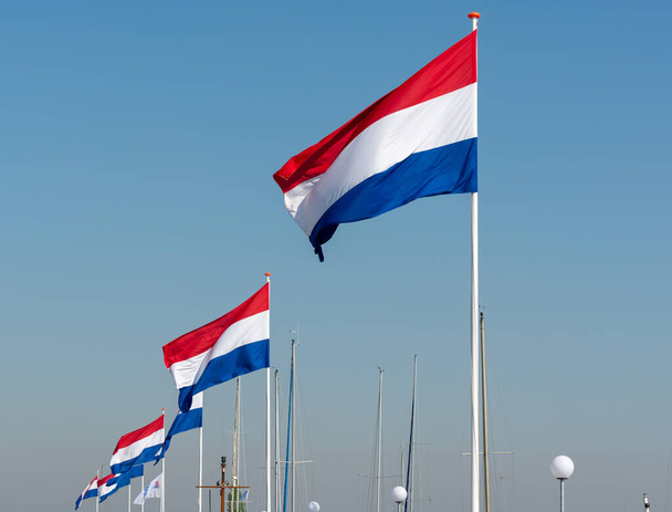Bandeiras do Reino dos Países Baixos, bandeira nacional holandesa em três cores vermelho, branco e azul e azul céu fundo
 - Foto, Imagem