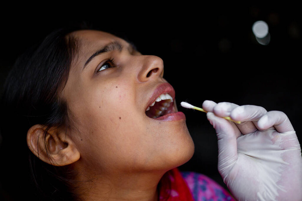 Doktorova ruka podstupuje test slin z úst mladé ženy s bavlněným tamponem. Koronavirus Odběr vzorků hrdla. Pohled zblízka. - Fotografie, Obrázek