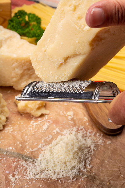 Man cooking with hard italian cheese, grated parmesan or grana padano cheese, hand with cheese grater - Photo, Image