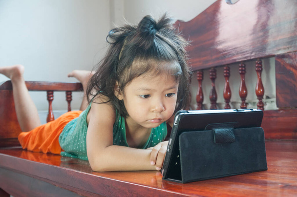 Молода дівчина лежить на дерев'яному стільці і навчається онлайн курсу на бездротовому цифровому планшеті, перебуваючи вдома в ситуації Corona Virus або Covid 19 спалаху. - Фото, зображення