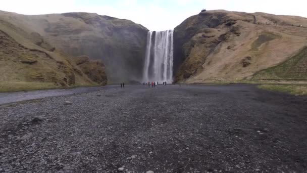 Skogafossin vesiputous Etelä-Islannissa, kultaisella kehällä. Vierailijat tulivat katsomaan vesiputousta, turistit kävelevät vuoren juurella. - Materiaali, video