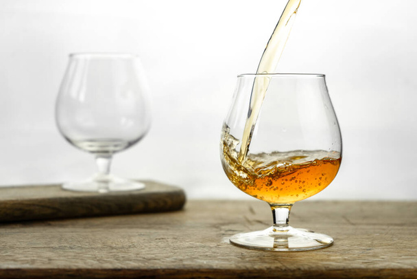 Cognac\ Whiskey in Cognac-Glas auf Holztisch, goldene Spirituosen auf weißem Hintergrund - Foto, Bild