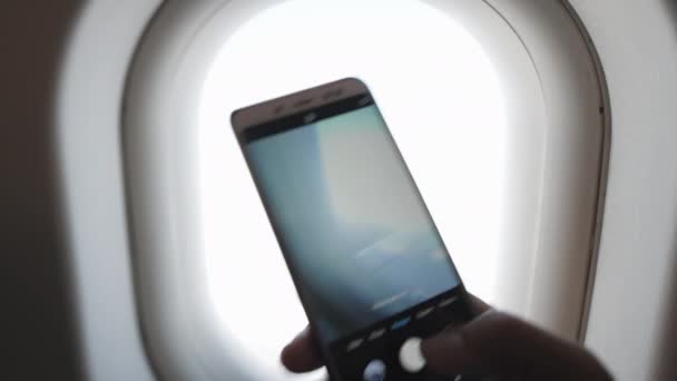 Mies ottaa kuvia siiven lentokoneen ja lentokoneen moottorin porthole ikkunasta kameran älypuhelimet valkoinen. - Materiaali, video