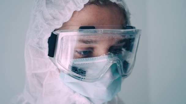close-up of the face of a nurse dressed in protective coveralls, mask and glasses expels the remnants of air from a medical syringe with a vaccine, slow-motion shooting - Video