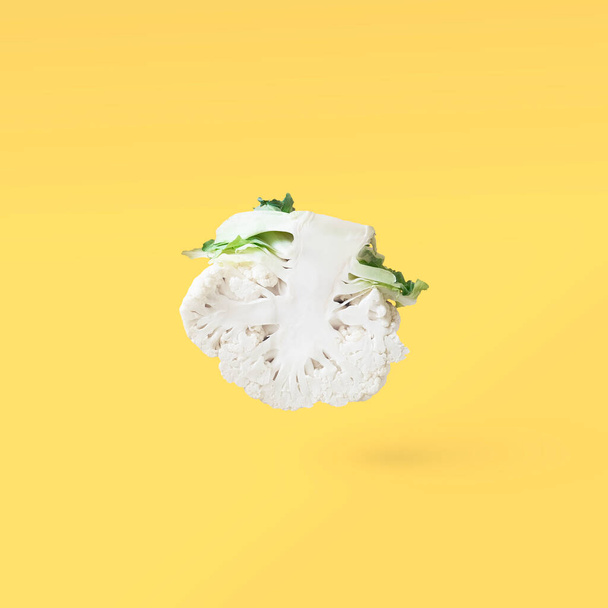 Half a head of cut cauliflower closeup soars in the air on a yellow background with a shadow. Creative flying food concept.Square minimalistic vegetable background with free copy space for text. - Foto, afbeelding