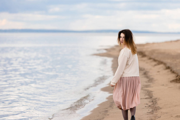Ένα νεαρό όμορφο κορίτσι περπατά κατά μήκος της ακτής και κοιτάζει πίσω. - Φωτογραφία, εικόνα