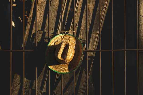 Chapéu de palha mexicano com borda verde na cerca de madeira marrom escuro iluminado pelo sol
 - Foto, Imagem
