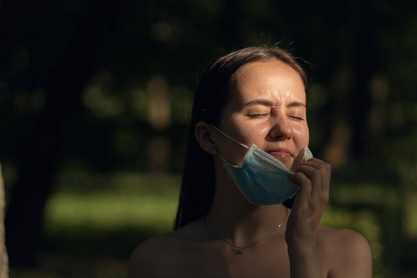 Mädchen ruhen sich an einem sonnigen Sommertag im Park aus. Porträt einer Frau, die ihre Gesichtsmaske abnimmt. - Foto, Bild