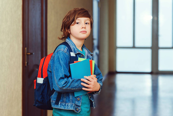 Νεαρός μαθητής με σχολική τσάντα και σημειωματάρια. Έξυπνο σχολιαρόπαιδο που κοιτάει την κάμερα. Εκπαιδευτική ιδέα. Πίσω στο σχολείο. Ο μαθητής πάει στην τάξη. Χαριτωμένο αγόρι σχολείο με σακίδιο. - Φωτογραφία, εικόνα
