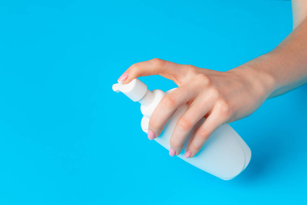 Female hand holding skincare product bottle on blue - 写真・画像
