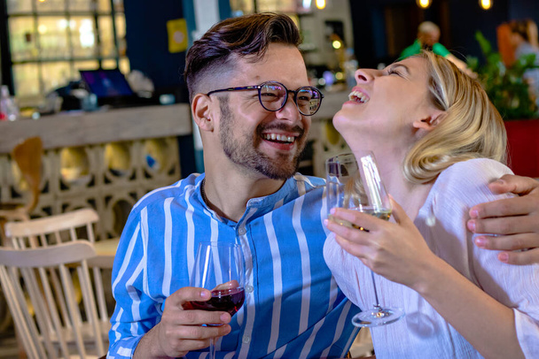  Onnellinen nuori romanttinen pari nauraa ja paahtoleipää viinilasien kanssa illallisella kauniissa hienossa ravintolassa. - Valokuva, kuva