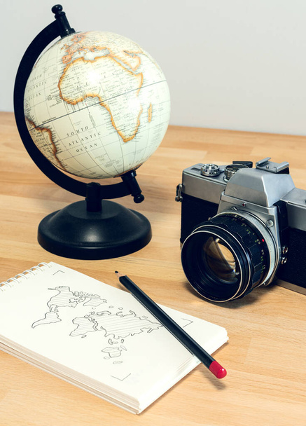 Κάμερα, υδρόγειο και σημειωματάριο με παγκόσμιο χάρτη σε ξύλινο γραφείο. Travel concept image: σχεδιασμός ταξιδιού. - Φωτογραφία, εικόνα