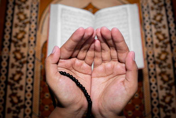 A fiatal muszlim nő Tasbeeh-vel imádkozik. A Szent Korán a háttér, a beltérben. Koncentrálj a kezekre.. - Fotó, kép