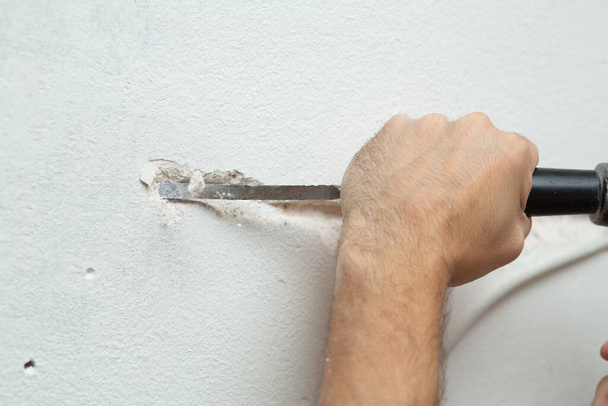 Reparación del local. Un hombre hace una zanja para poner cable en la pared. Instalación de cableado eléctrico en la pared
 - Foto, Imagen