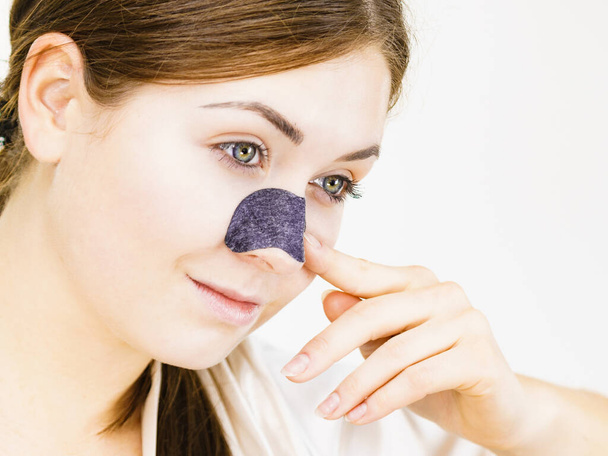 Woman appying clear-up strips on nose, using pore cleansing textile mask, on white. Girl taking care of skin complexion. Beauty treatment. Skincare. - Fotó, kép