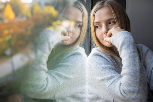 Depressed/anxious young woman sitting by a large window, feeling blue, sad, uncertain - Valokuva, kuva