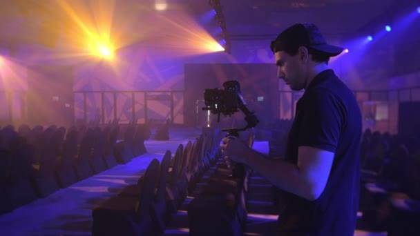 Ein junger, attraktiver Mann mit einem Drei-Achsen-Stabilisator und einer DSLR-Kamera mit Lichtkegel macht ein filmisches Video. - Filmmaterial, Video