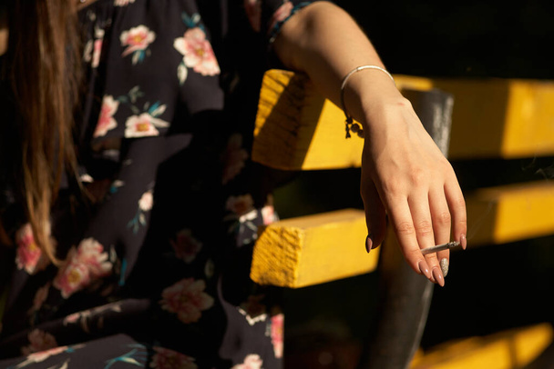 Крупним планом жіноча рука з цигаркою в парку. Концепція куріння тютюну в громадському місці, шкоди здоров'ю та іншим, залежності та раку
. - Фото, зображення