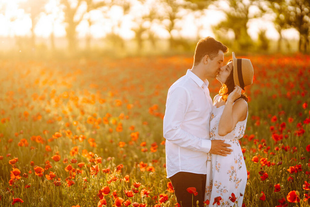Loving couple in the poppy field. Loving couple hug one another during romantic date in poppy field. Enjoying time together. The concept of youth, love and lifestyle. - Photo, Image