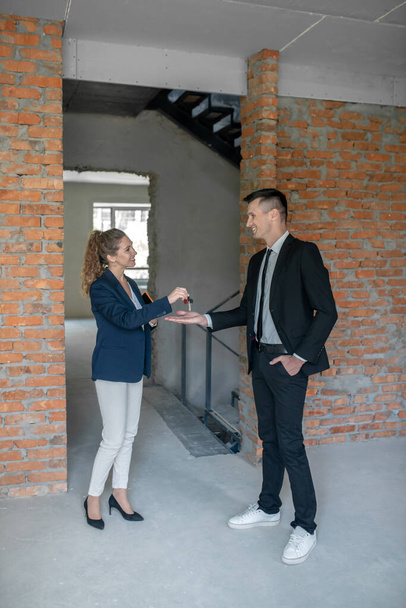 Female broker giving the key to the tall man in a suit - Photo, Image