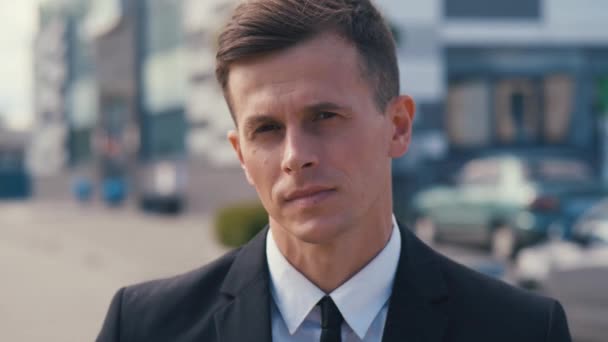 Portrait of attractive man in business suit in looking into camera and smiling in the city outdoors. Portrait of handsome male businessman standing outdoor near offices. - Footage, Video